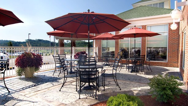 Une terrasse extérieure avec un sol en pierre, des chaises en métal noir et des parasols rouges.