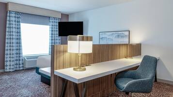 Een hotelkamer met een bureau, stoel, lamp, televisie en kunstwerk aan de muur.