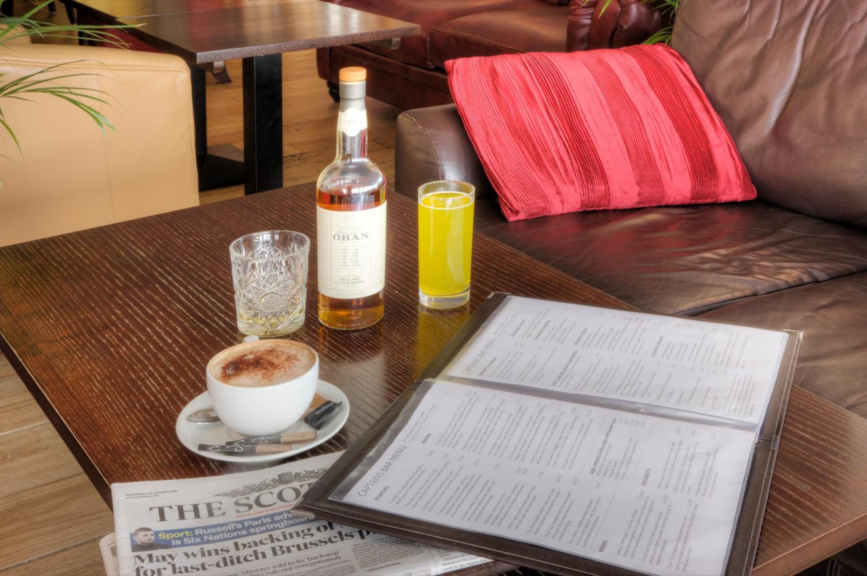 Una mesa con un menú, una botella de whisky OBN, un vaso de bebida amarilla y una taza de café.