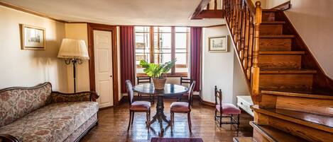 A traditional living room with a sofa, a dining table with chairs, a staircase, and a lamp.