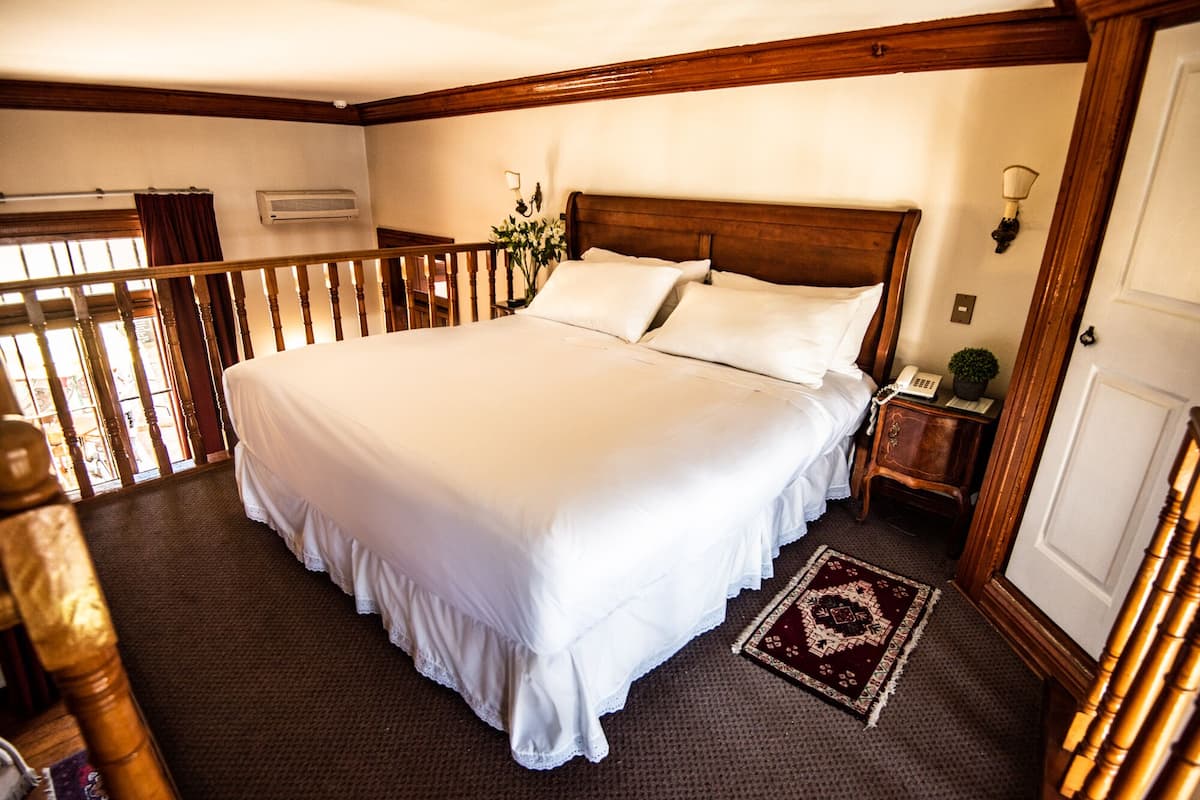 A large, neatly made bed in a room with wooden beams and a balcony.