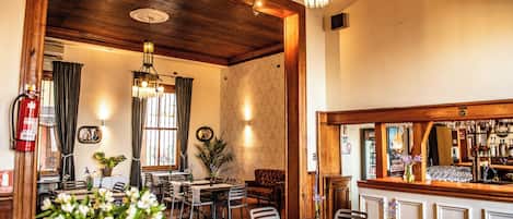 A dining area with wooden tables and chairs, a bar counter, and a chandelier.