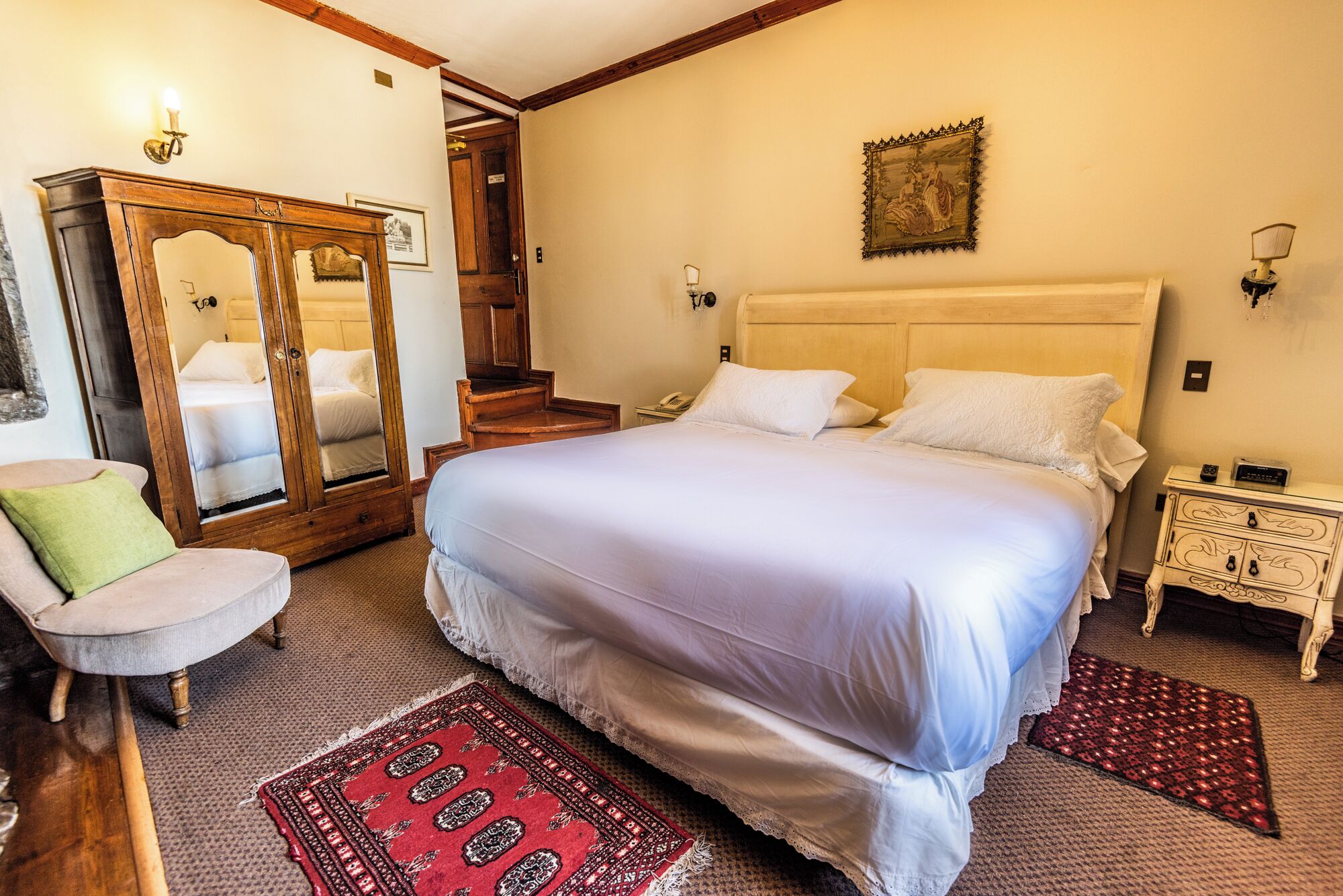 Une chambre avec un grand lit, une armoire en bois, une chaise et une petite table de chevet avec une lampe.