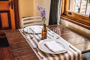 Una mesa de comedor dispuesta con platos, vasos, cubiertos y un florero con flores.