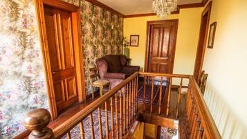Una escalera con balaustres de madera y barandilla, que conduce a un rellano con una araña y una alfombra estampada.