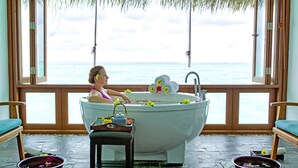 A bathtub with a view of the sea, a wooden chair, and a stone floor.