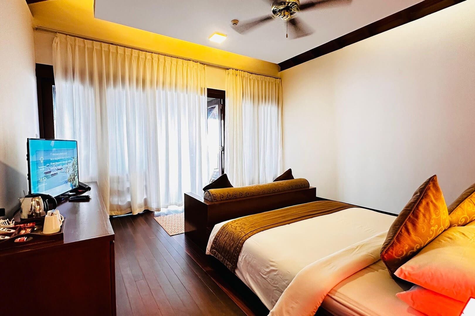 A hotel room with a bed, a desk with a computer, a ceiling fan, and curtains.