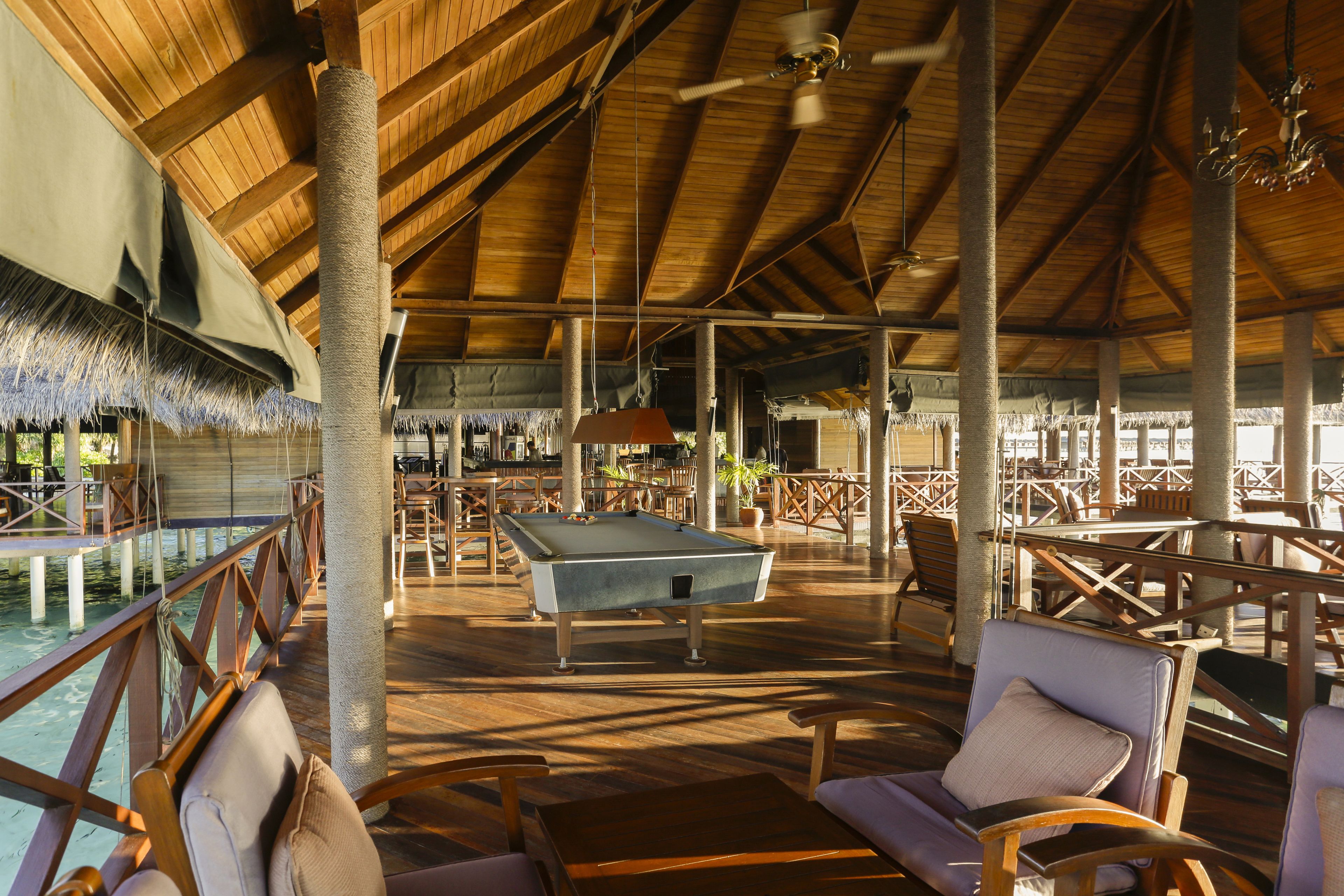 A spacious indoor area with a pool table, wooden furniture, and a thatched roof structure.