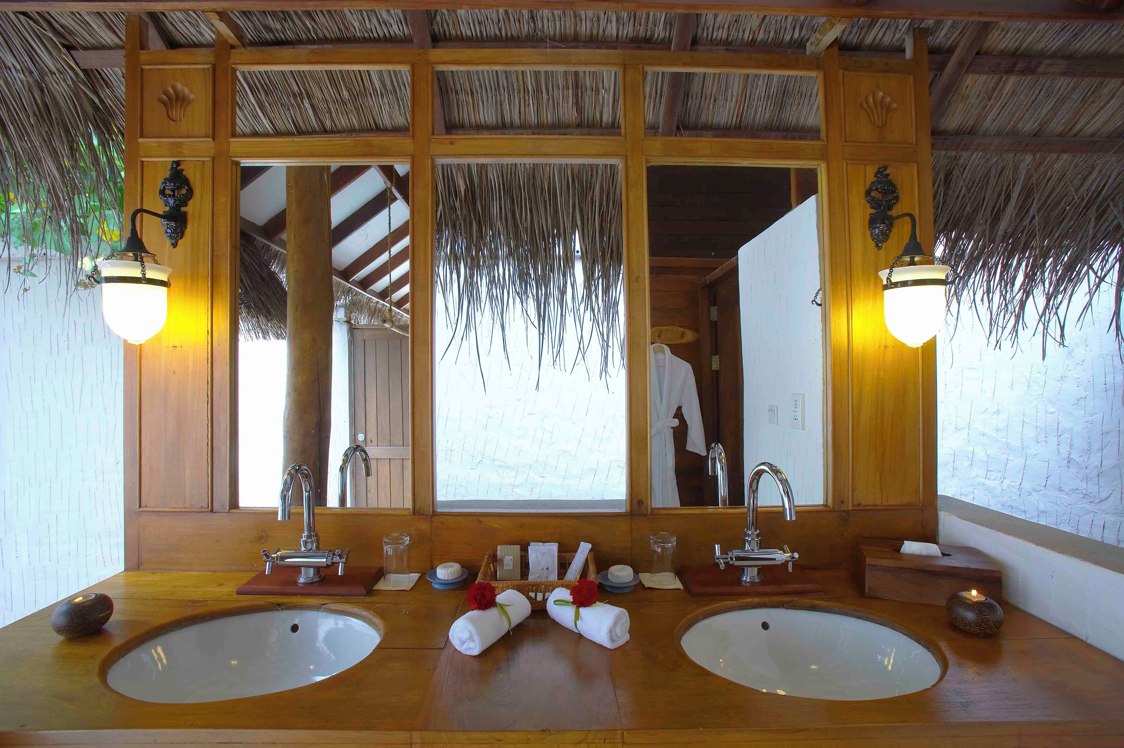 A bathroom with two sinks, a large mirror, and a thatched roof.