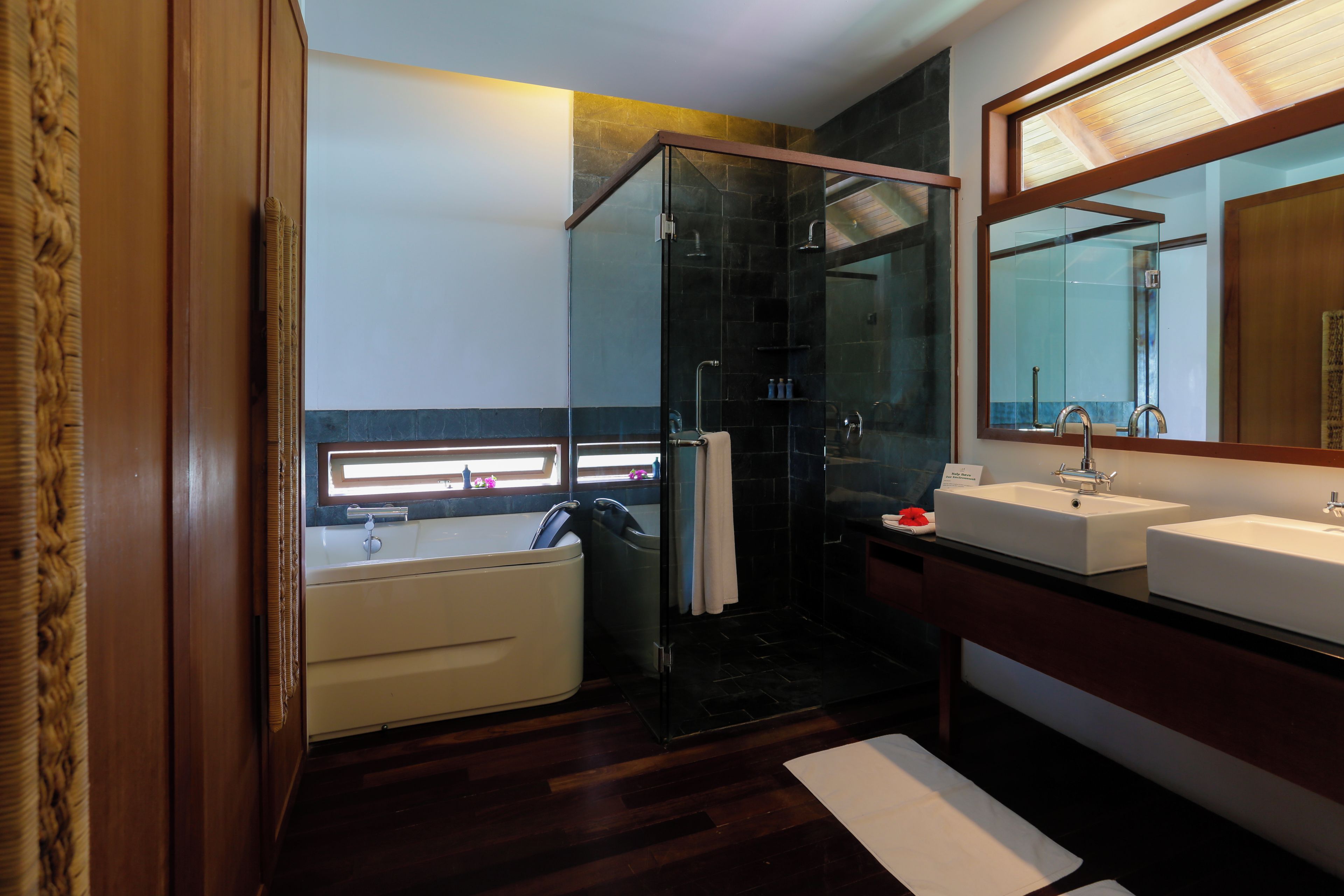 A modern bathroom with a glass-enclosed shower, a bathtub, and two sinks.