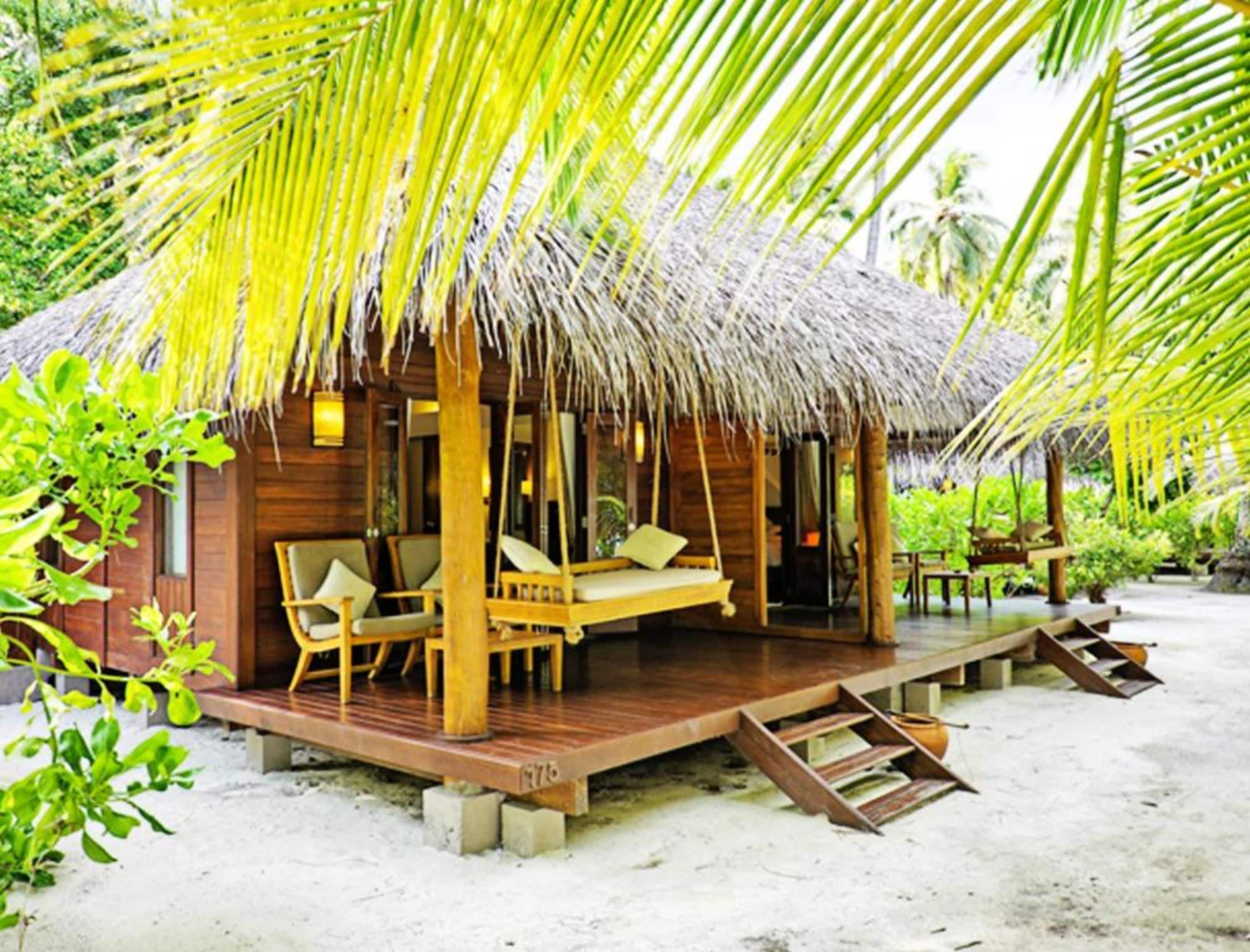 Een houten constructie met rieten dak, een houten terras en een bed met hemelbed.