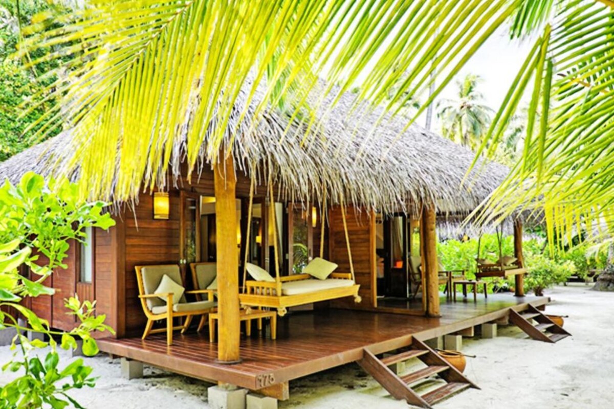 Une structure en bois avec un toit de chaume, une terrasse en bois et un lit à baldaquin.