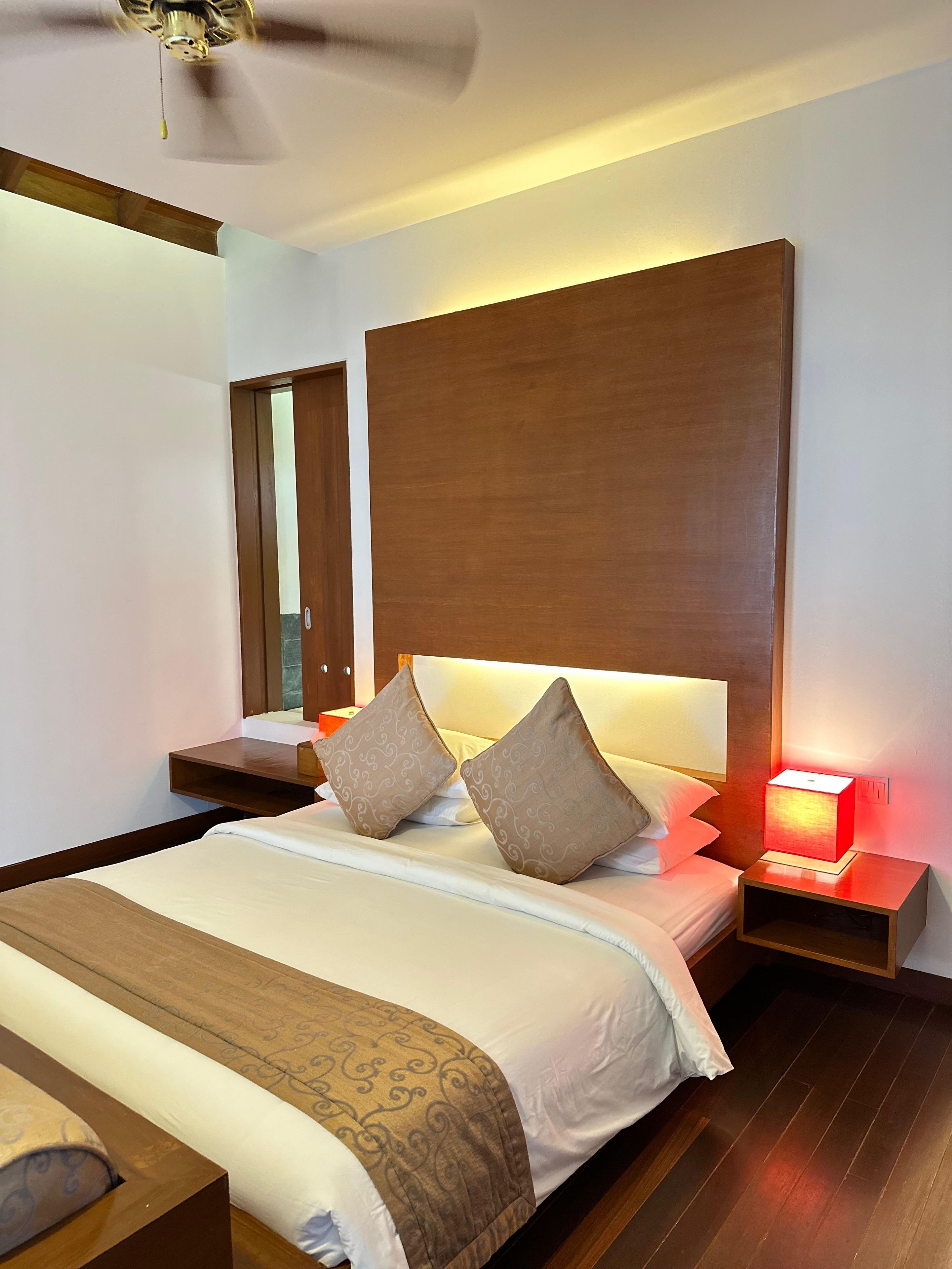 A hotel room with a large bed, a bedside table with a lamp, and a ceiling fan.