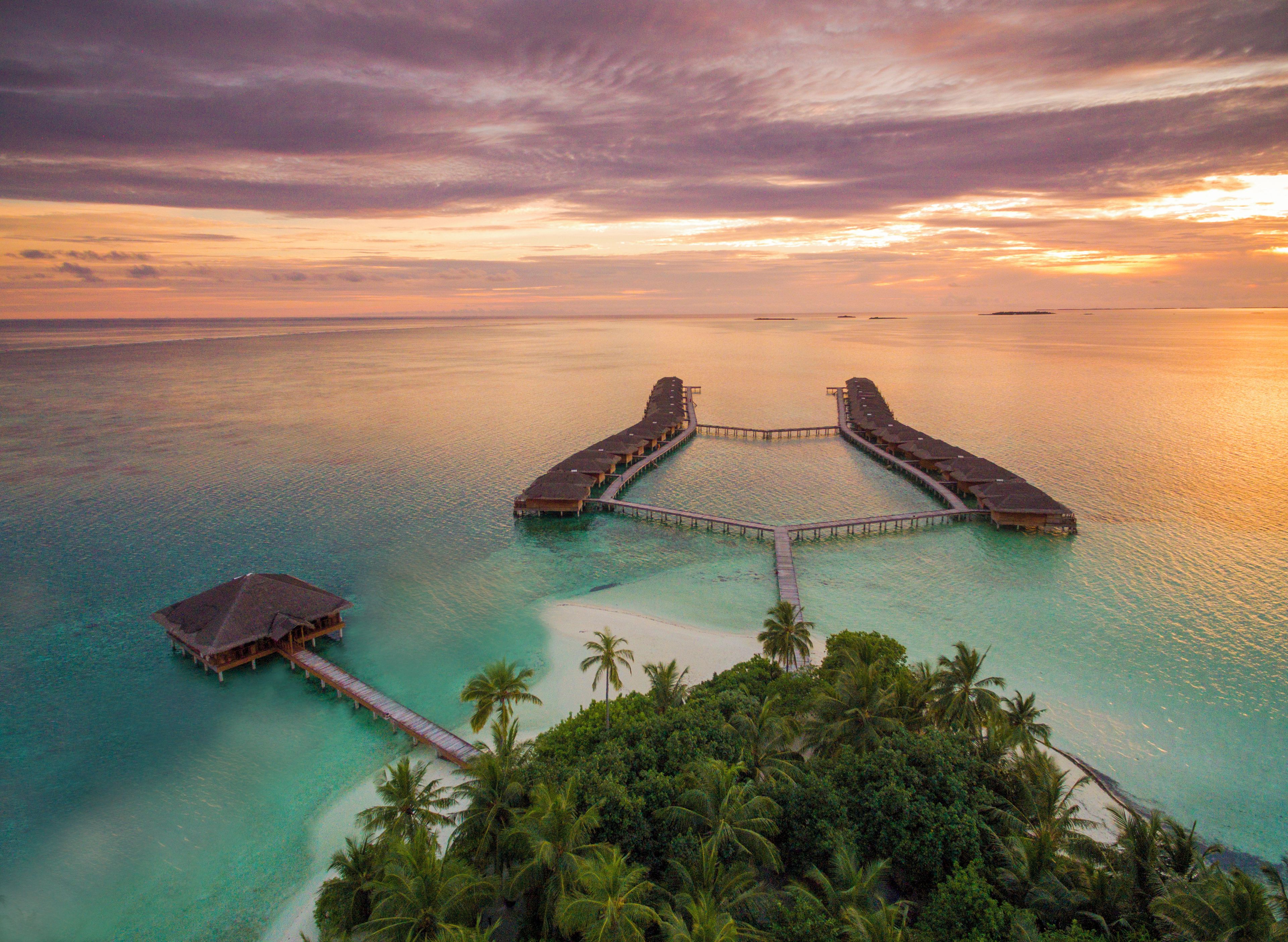Vista aérea de un resort con bungalows sobre el agua, unidos por pasarelas.