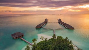 Vista aérea de un resort con bungalows sobre el agua, unidos por pasarelas.