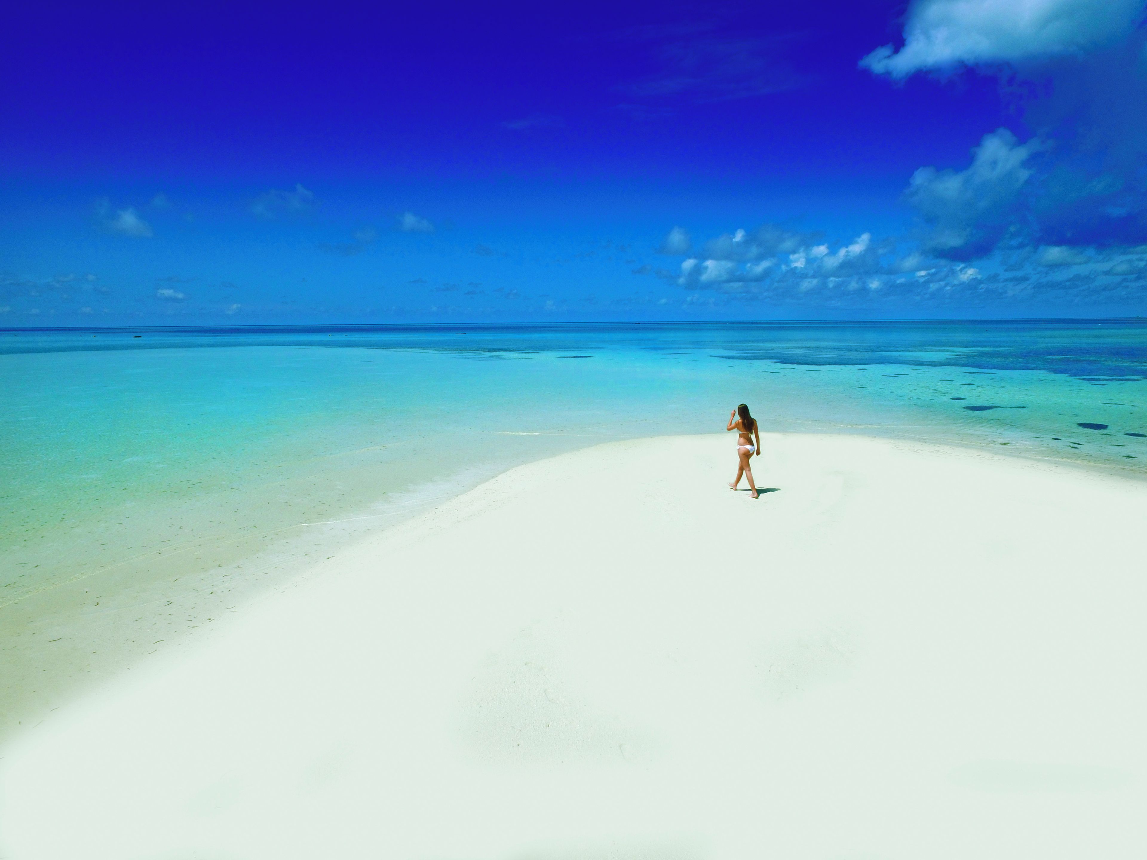 A person standing on a white sandy beach with clear blue water and a blue sky.