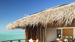 A wooden deck with two striped lounge chairs, a thatched-roof structure, and a view of the ocean.