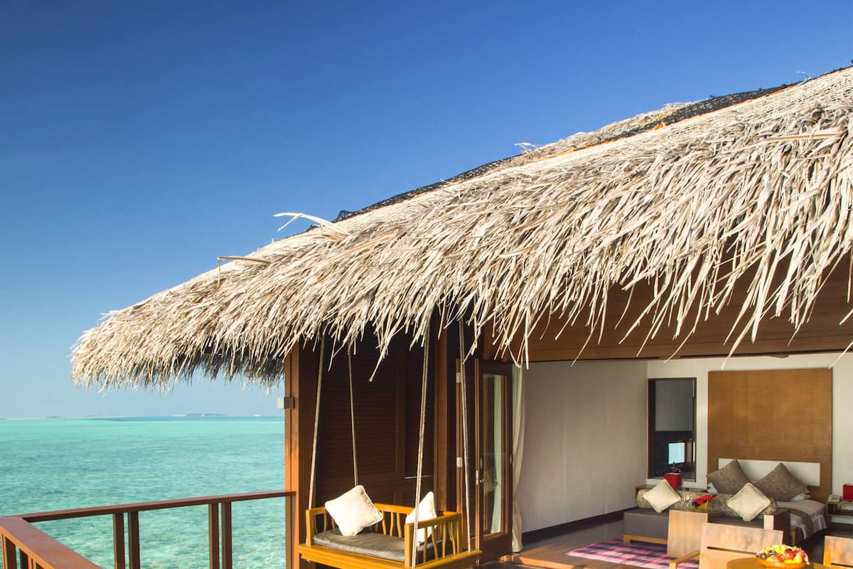 Una terraza de madera con dos sillones de playa a rayas, una estructura con techo de paja y vista al océano.