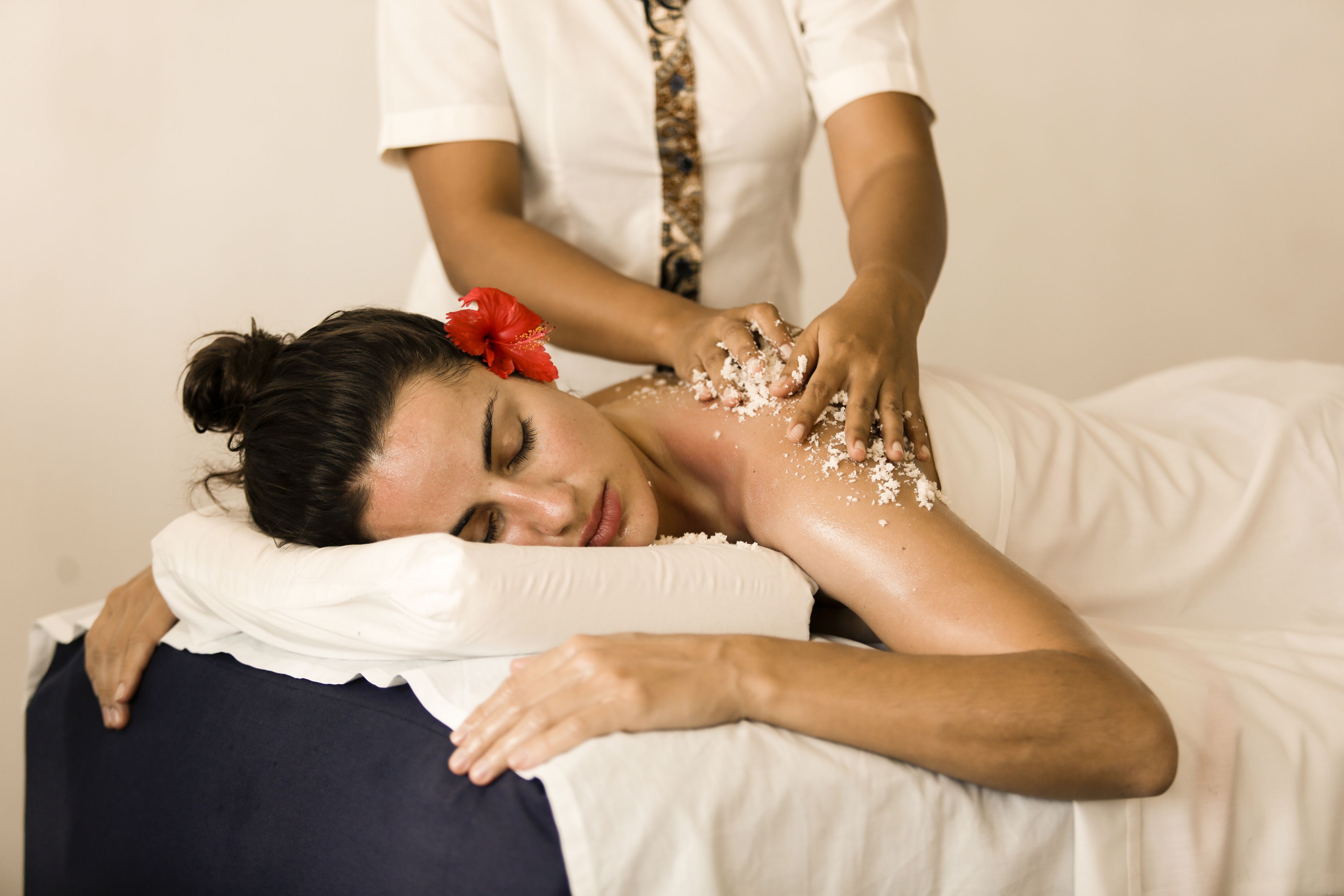 A person receiving a massage in a room with a white bed and a plain wall.