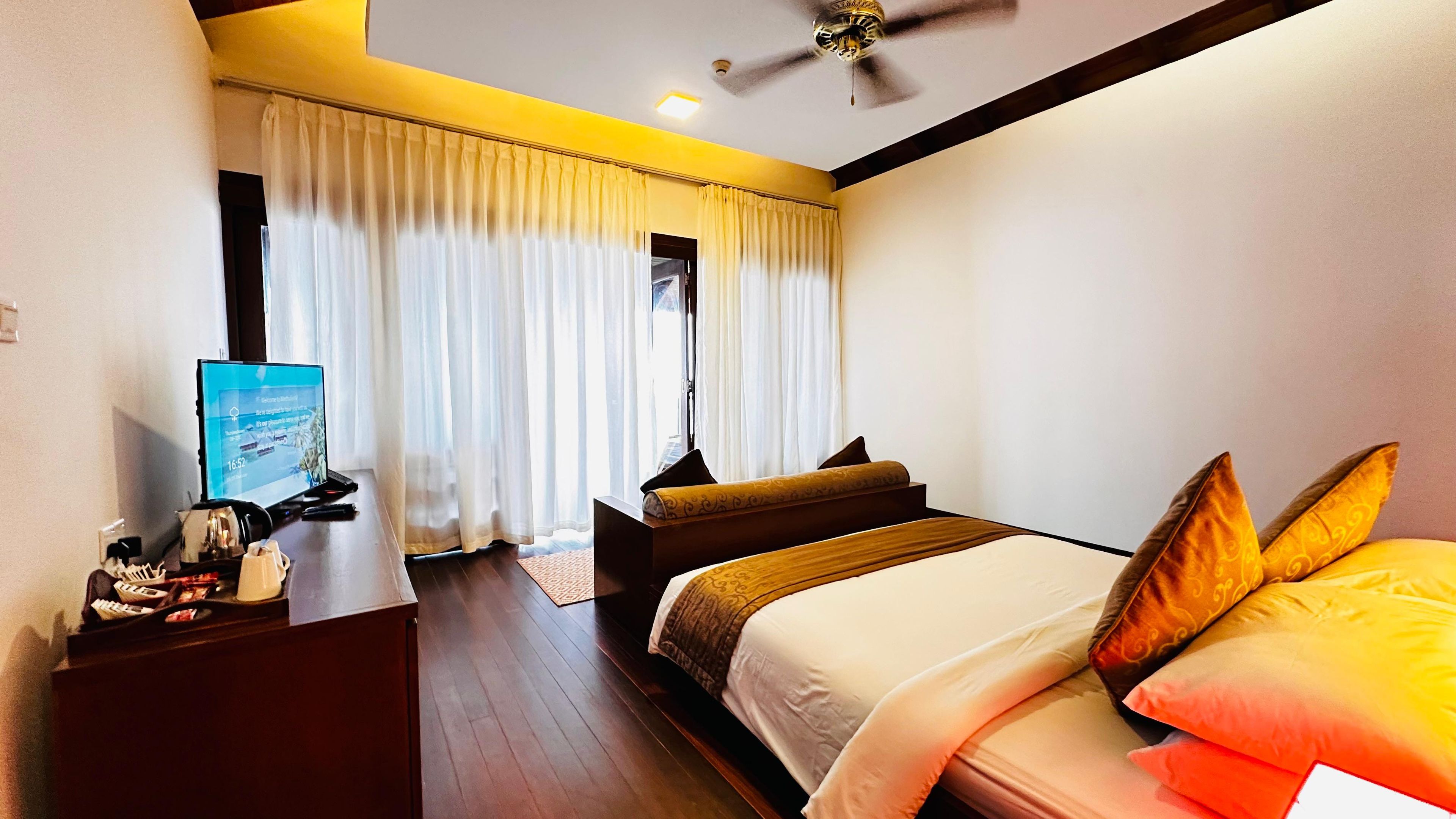 A hotel room with a bed, a desk with a computer, and a window with curtains.