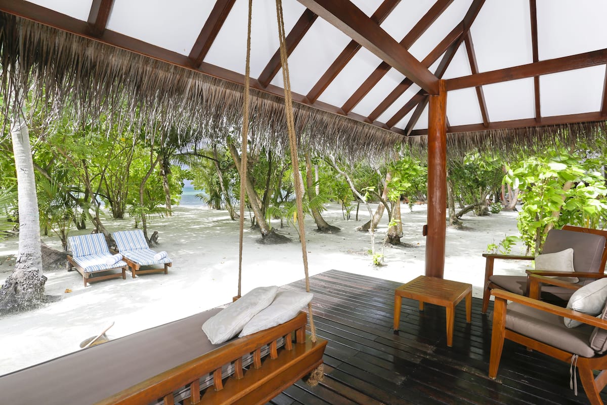 Un espacio de descanso al aire libre con mobiliario de madera, un columpio y vistas a una playa tropical.