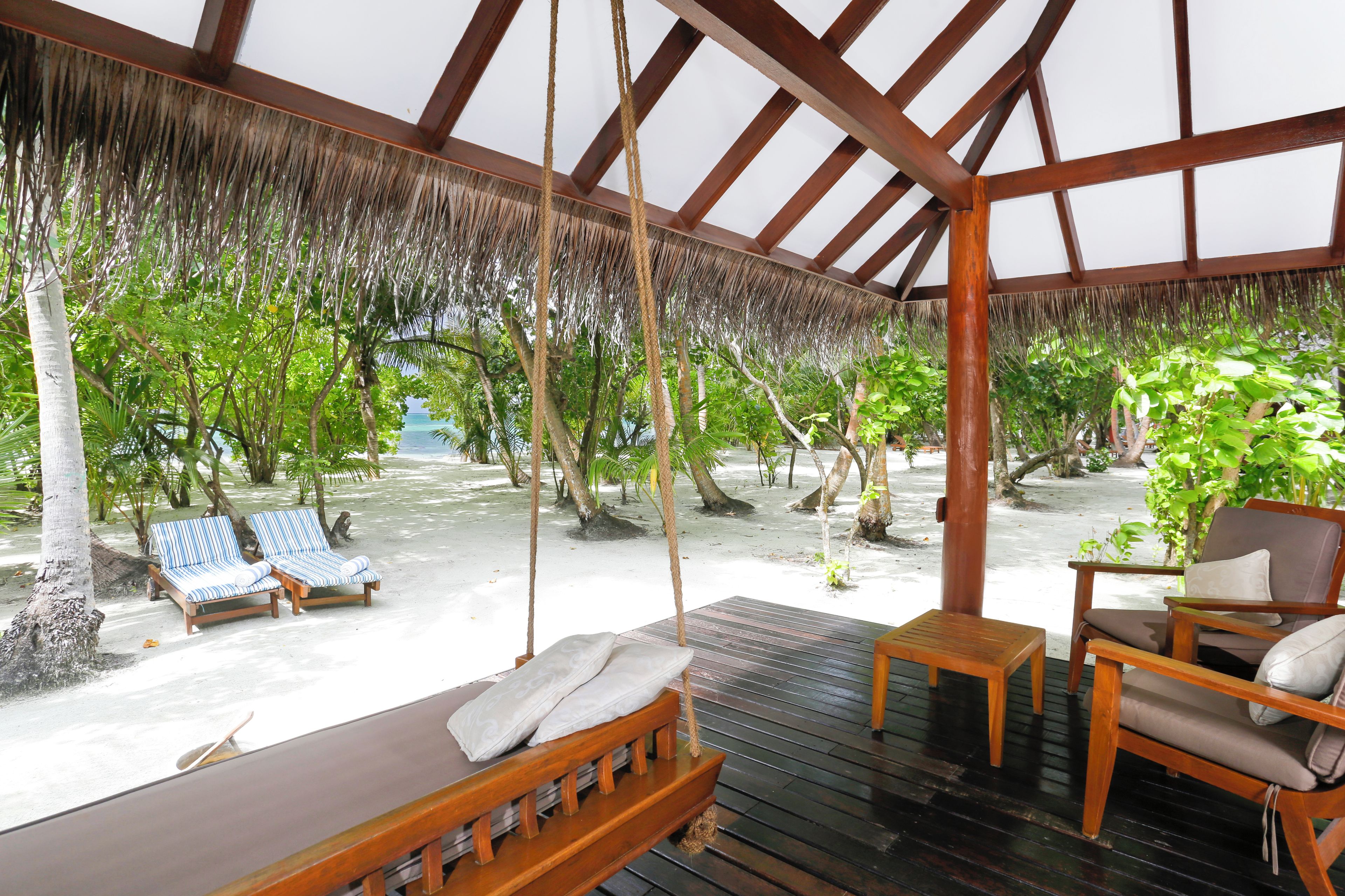 A covered outdoor seating area with wooden furniture and a thatched roof.