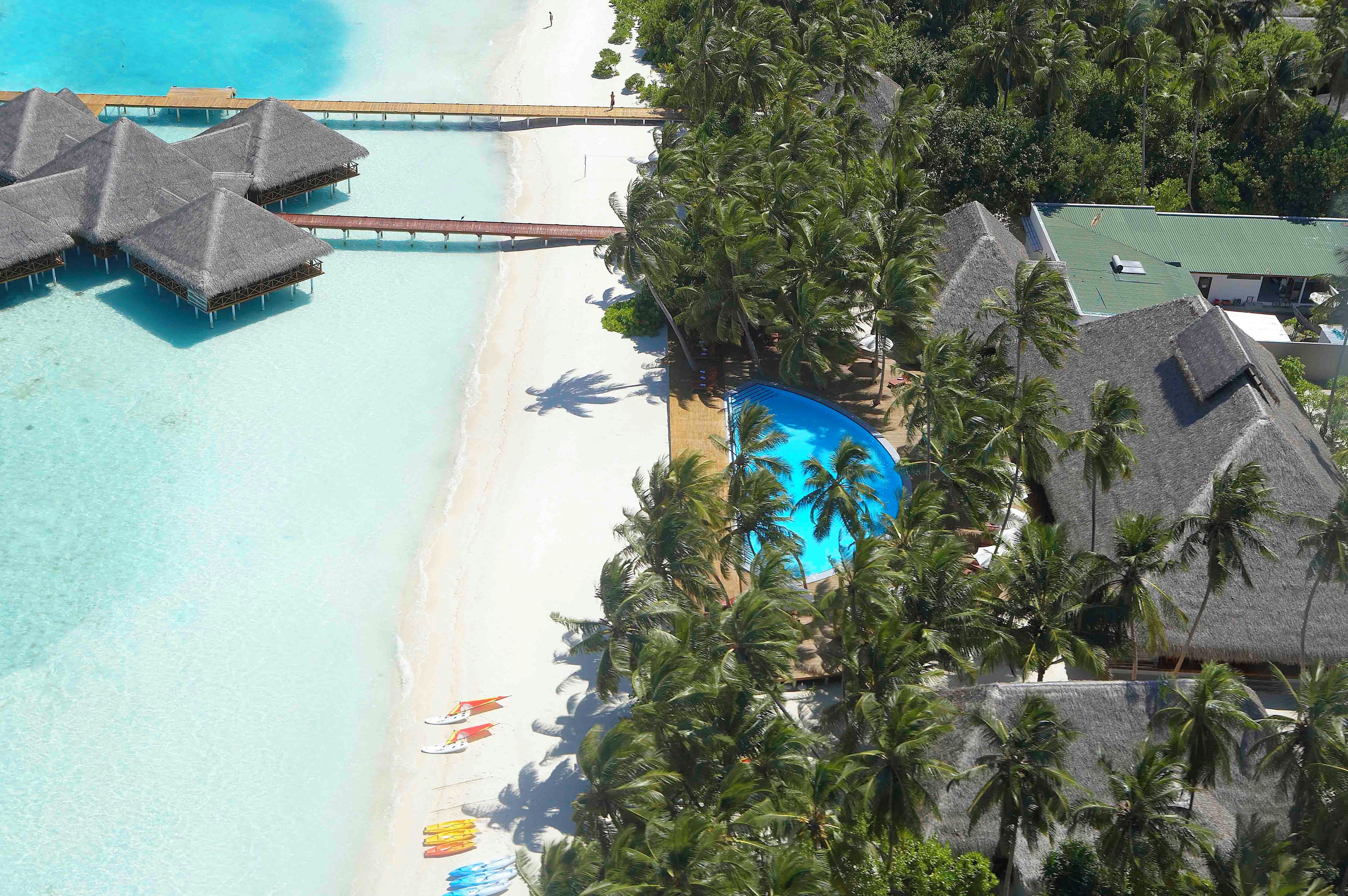 An aerial view of a resort with overwater bungalows, a beach, and a swimming pool.