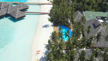 Een luchtbeeld van een resort met bungalows boven water, een strand en een zwembad.