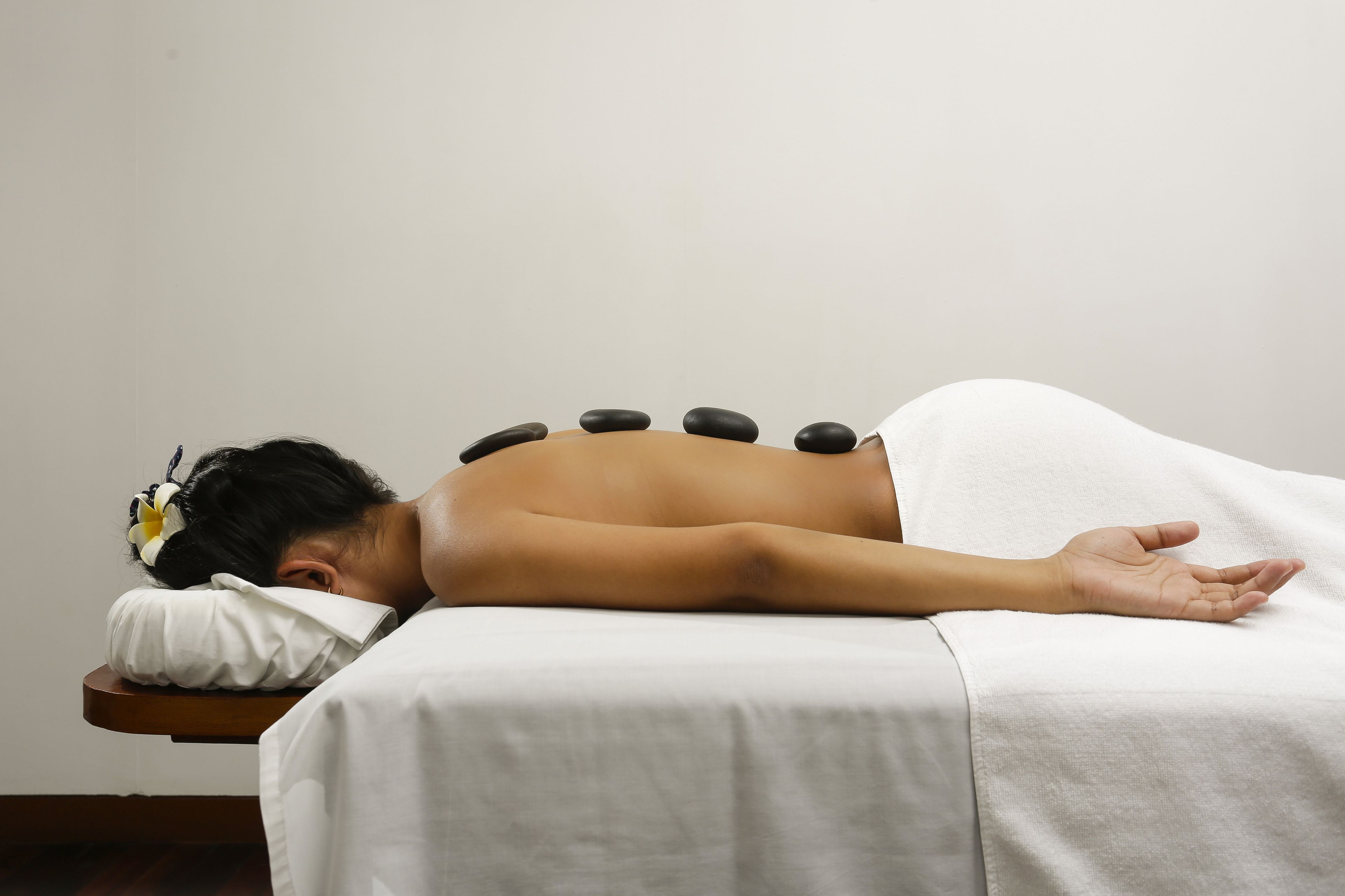 Iemand ontvangt een rugmassage met zwarte stenen op een bed.