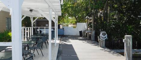 A covered outdoor patio with tables and chairs, a barbecue grill, and a wooden deck.