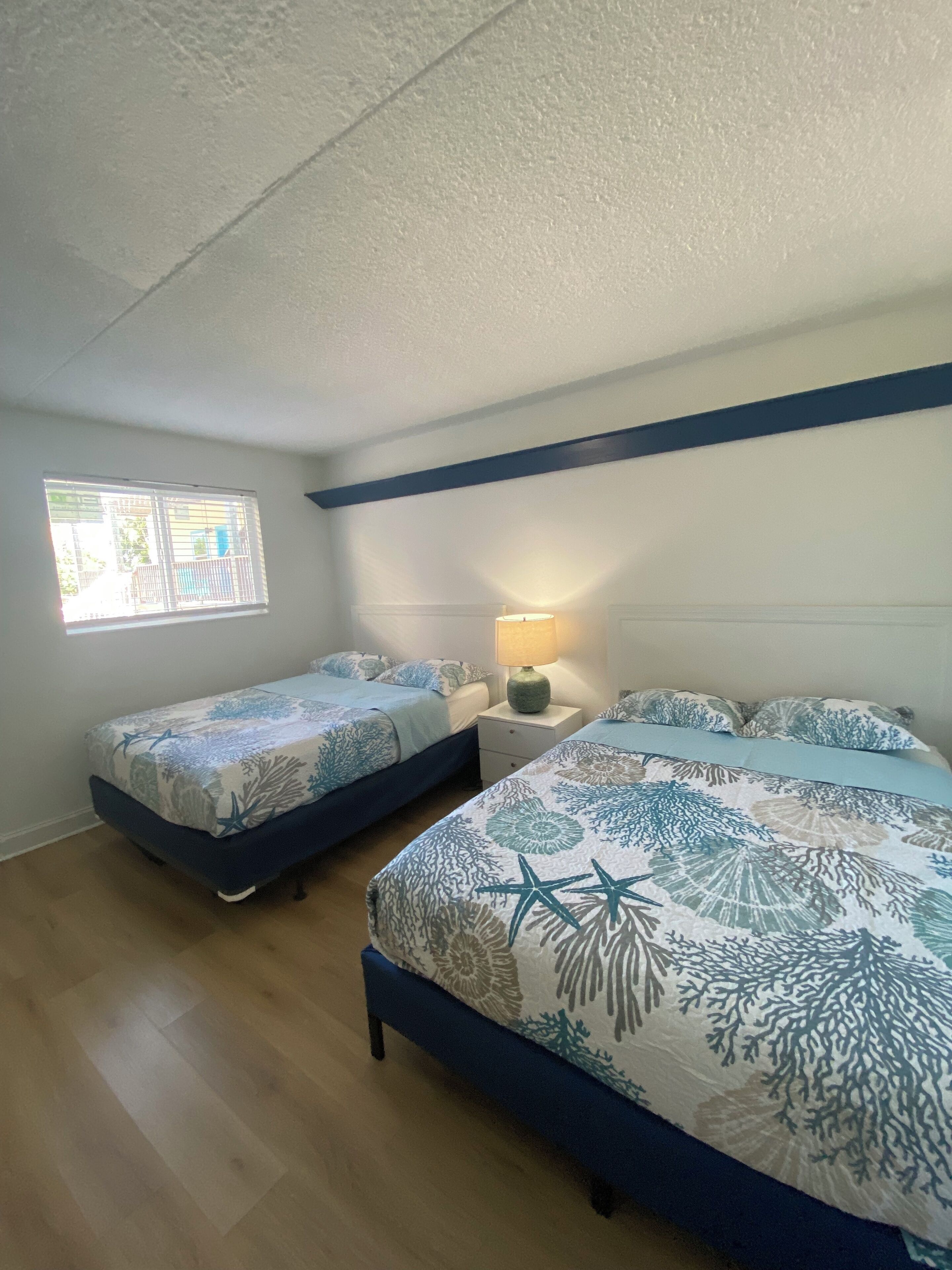 Un dormitorio con dos camas, una ventana y una mesita de noche con lámpara.
