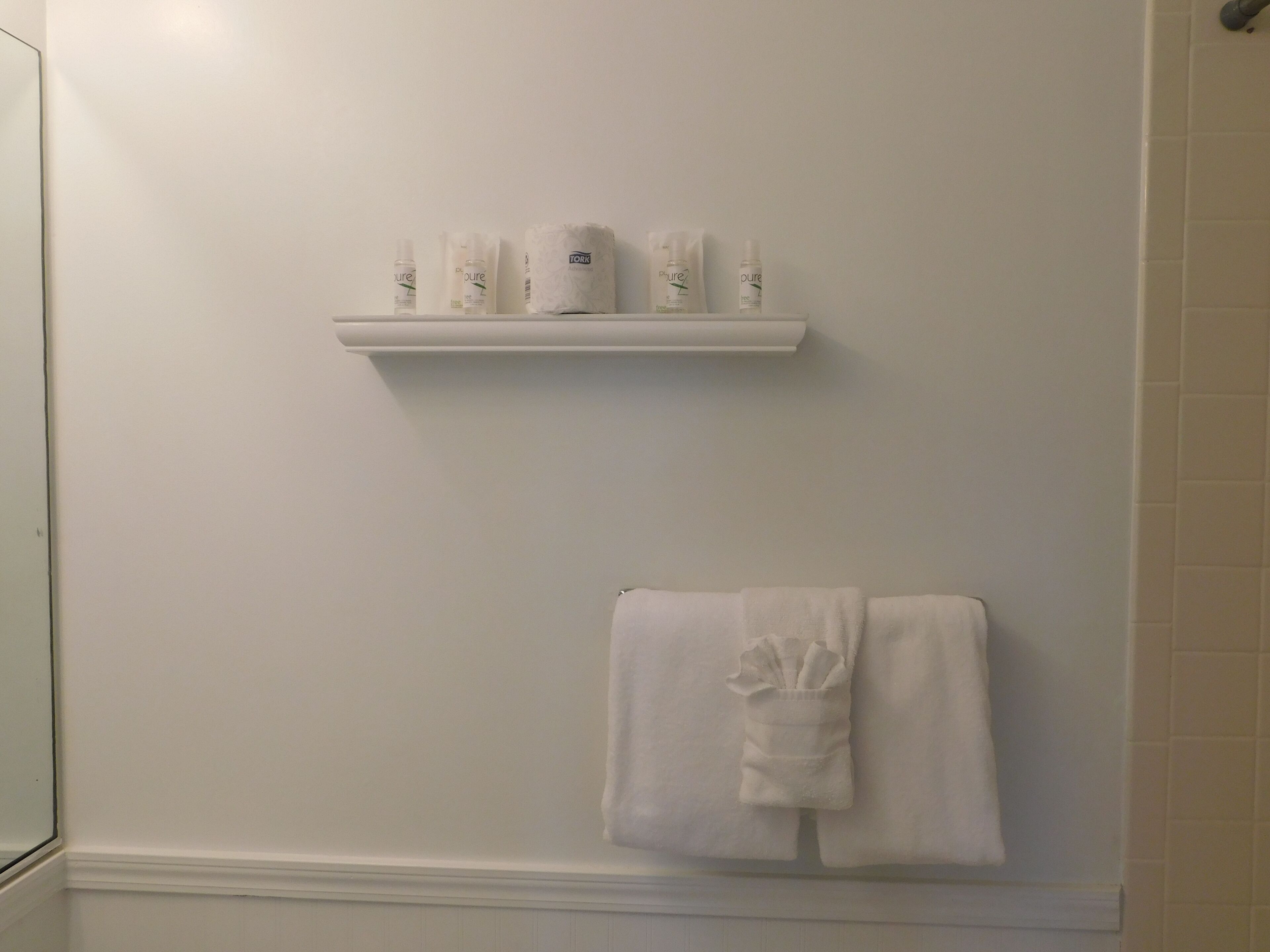 Un baño con pared blanca, un estante con artículos de aseo y una toalla colgada en un perchero.