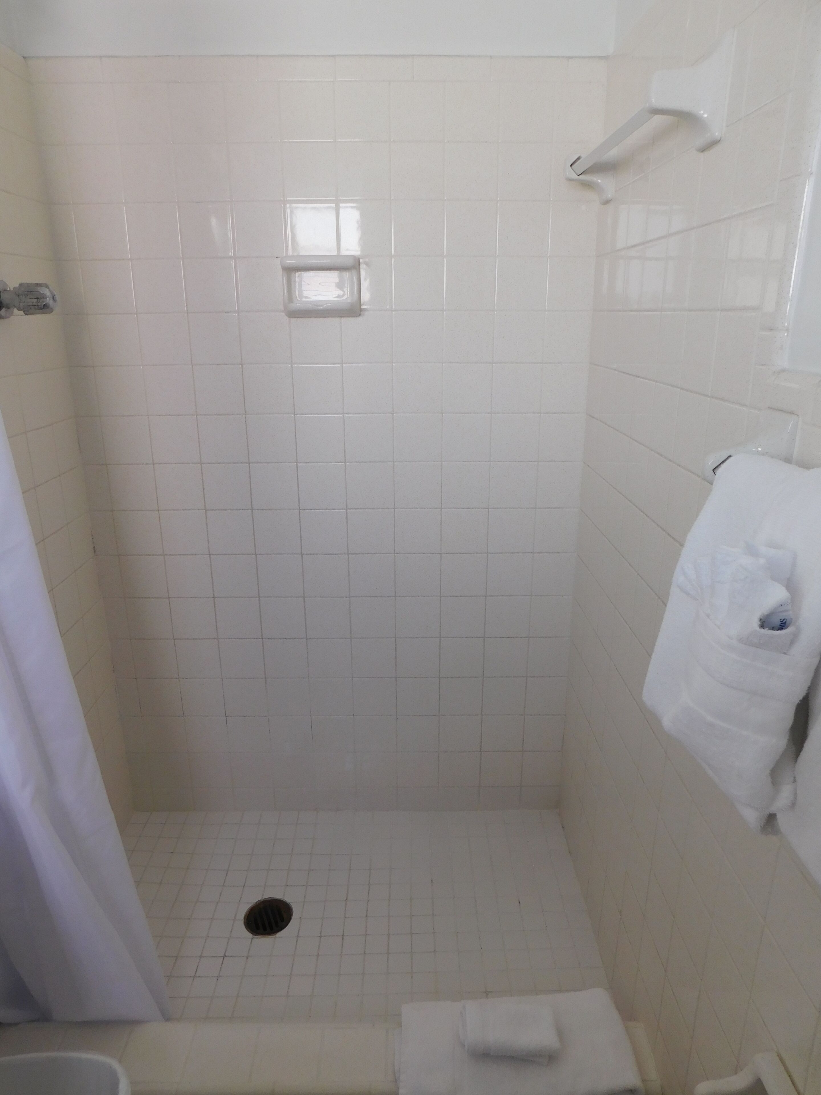 A small, tiled shower stall with a drain, a towel rack, and a shower curtain.