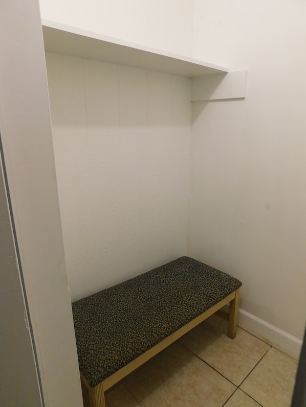 Um espaço pequeno e fechado, com um banco e uma prateleira branca.