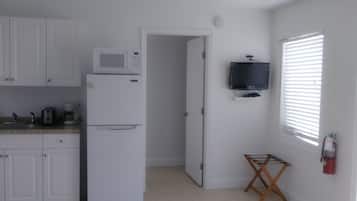 Una cocina con armarios blancos, microondas, refrigerador, ventilador de techo, televisor y ventana con persianas.