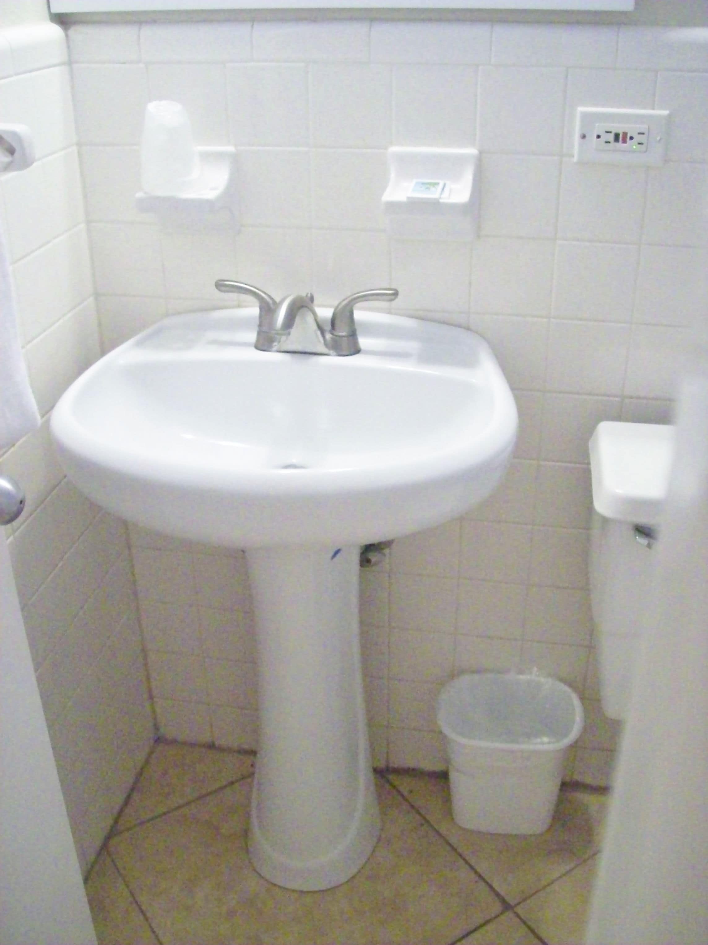 Une salle de bain avec un lavabo sur colonne, des toilettes et une poubelle.