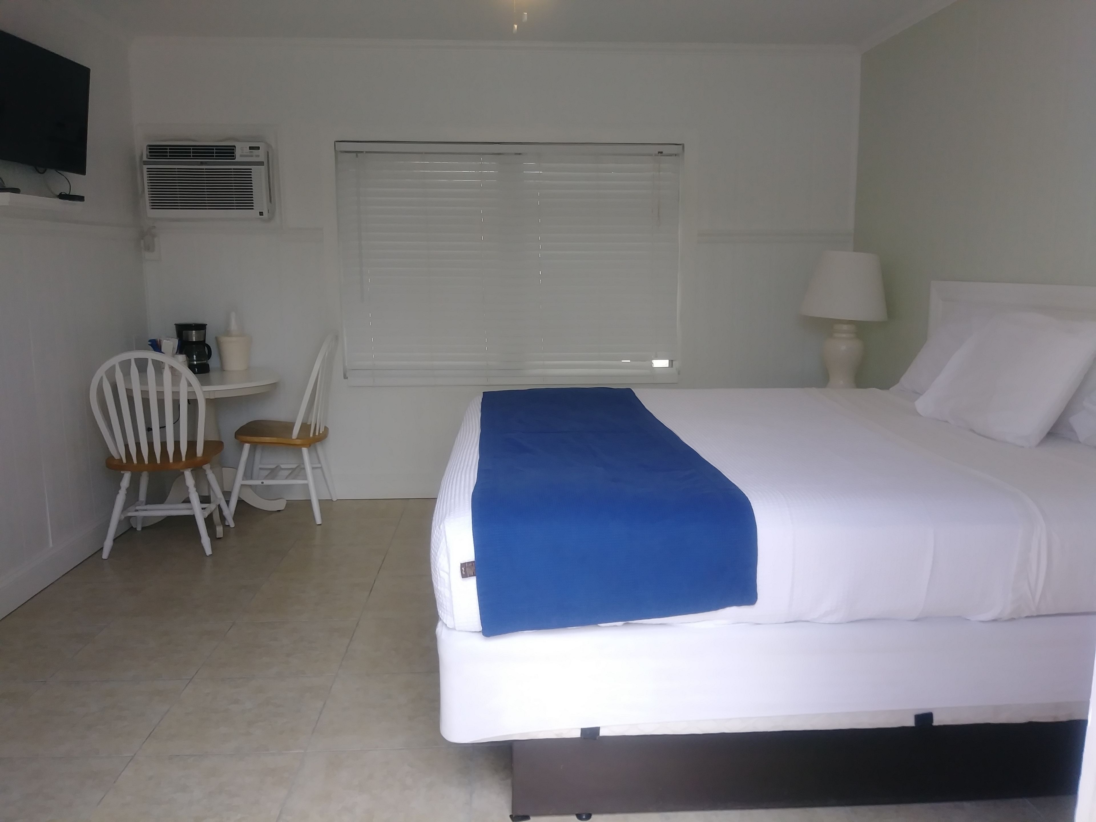 Un dormitorio con cama, escritorio con silla, ventana con persianas y equipo de aire acondicionado.