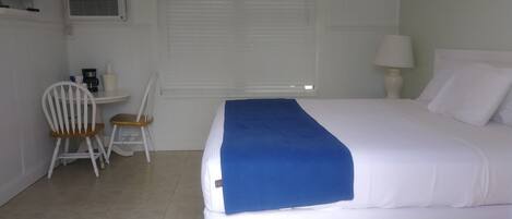 A bedroom with a bed, a desk with a chair, a window with blinds, and an air conditioning unit.