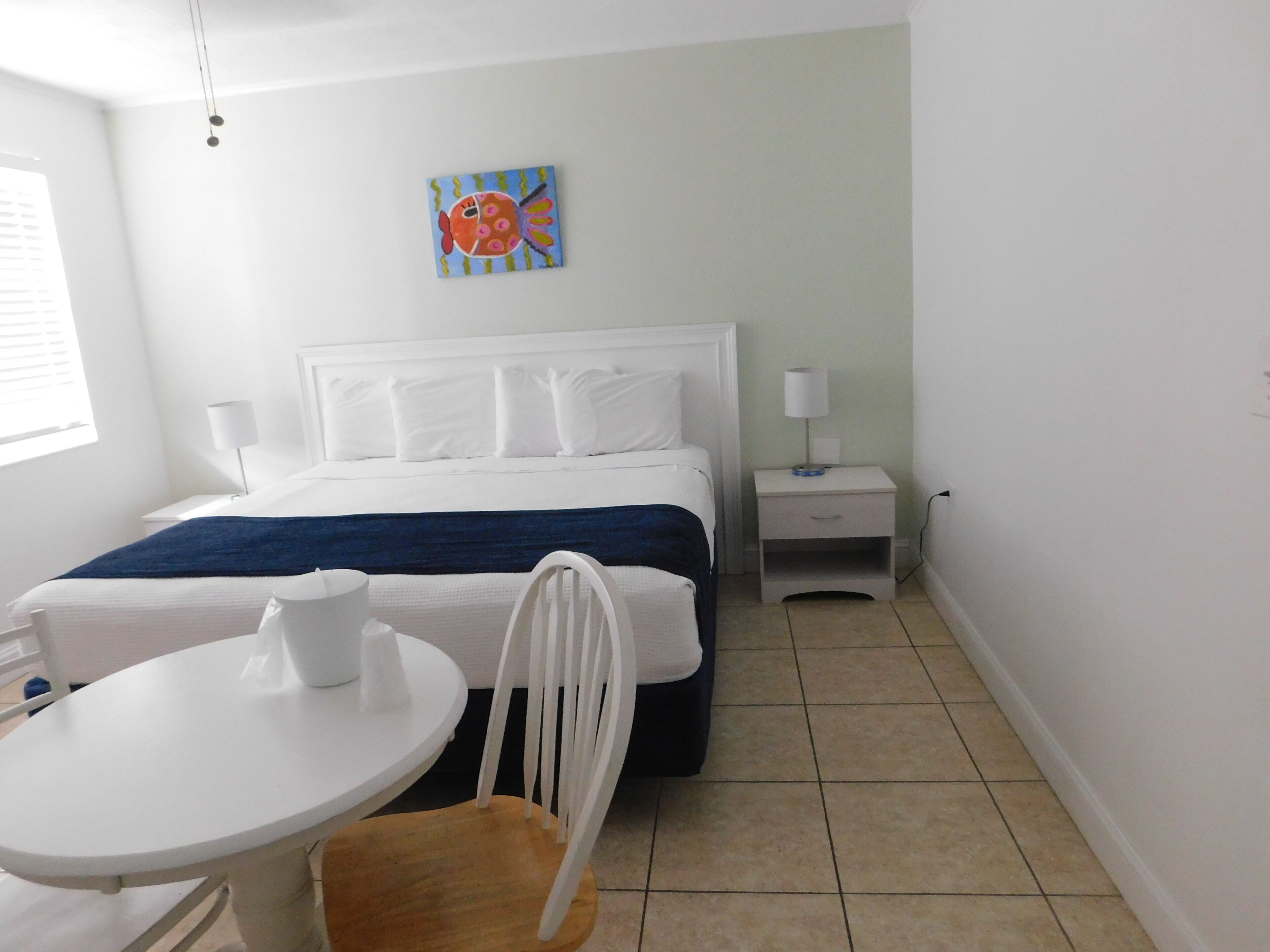 Une chambre d’hôtel avec un lit, une table de chevet, une chaise, une petite table et un tableau au mur.