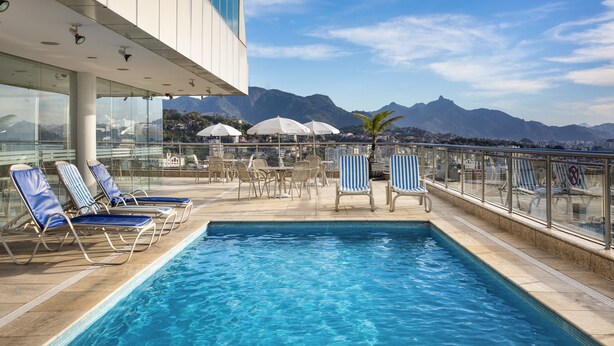 Una piscina en la azotea con sillas de descanso y sombrillas, con vistas a un paisaje montañoso.