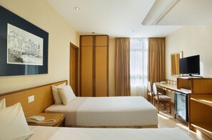 A hotel room with a bed, bedside table, a desk with a chair, a television, and a minibar. - Windsor Asturias Hotel (Rio de Janeiro)