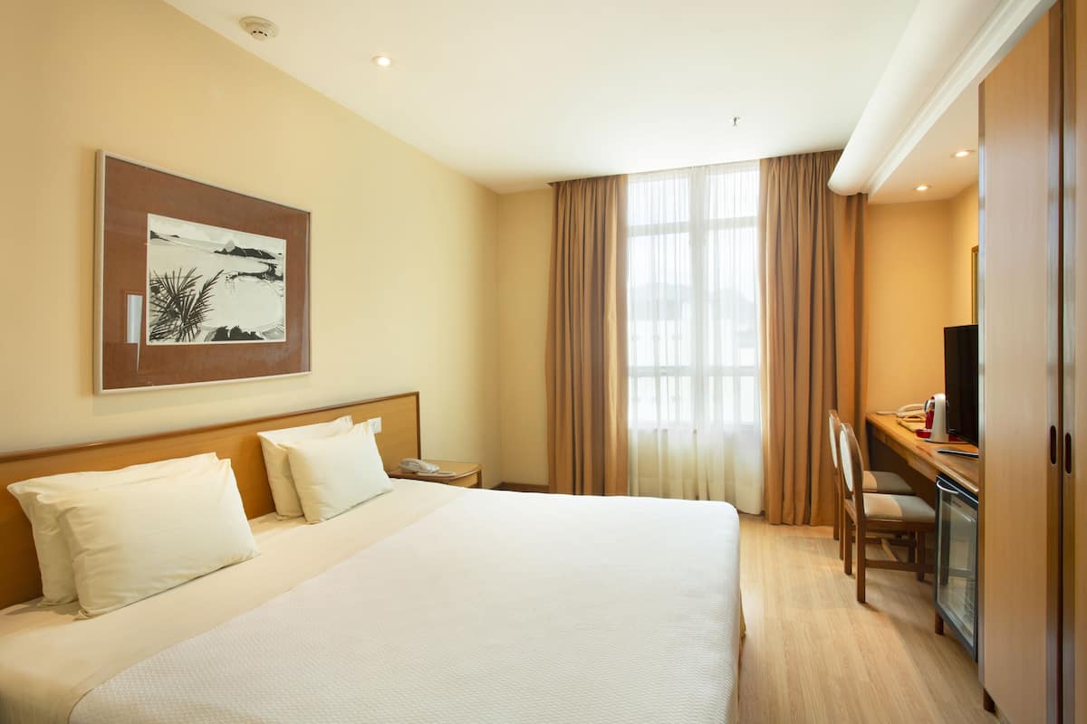 A hotel room with a large bed, a desk with a computer, a television, and a painting on the wall.