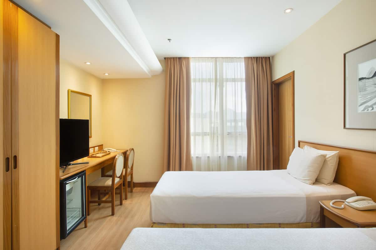 A hotel room with a bed, a desk with a computer, a TV, a phone, and a small fridge.