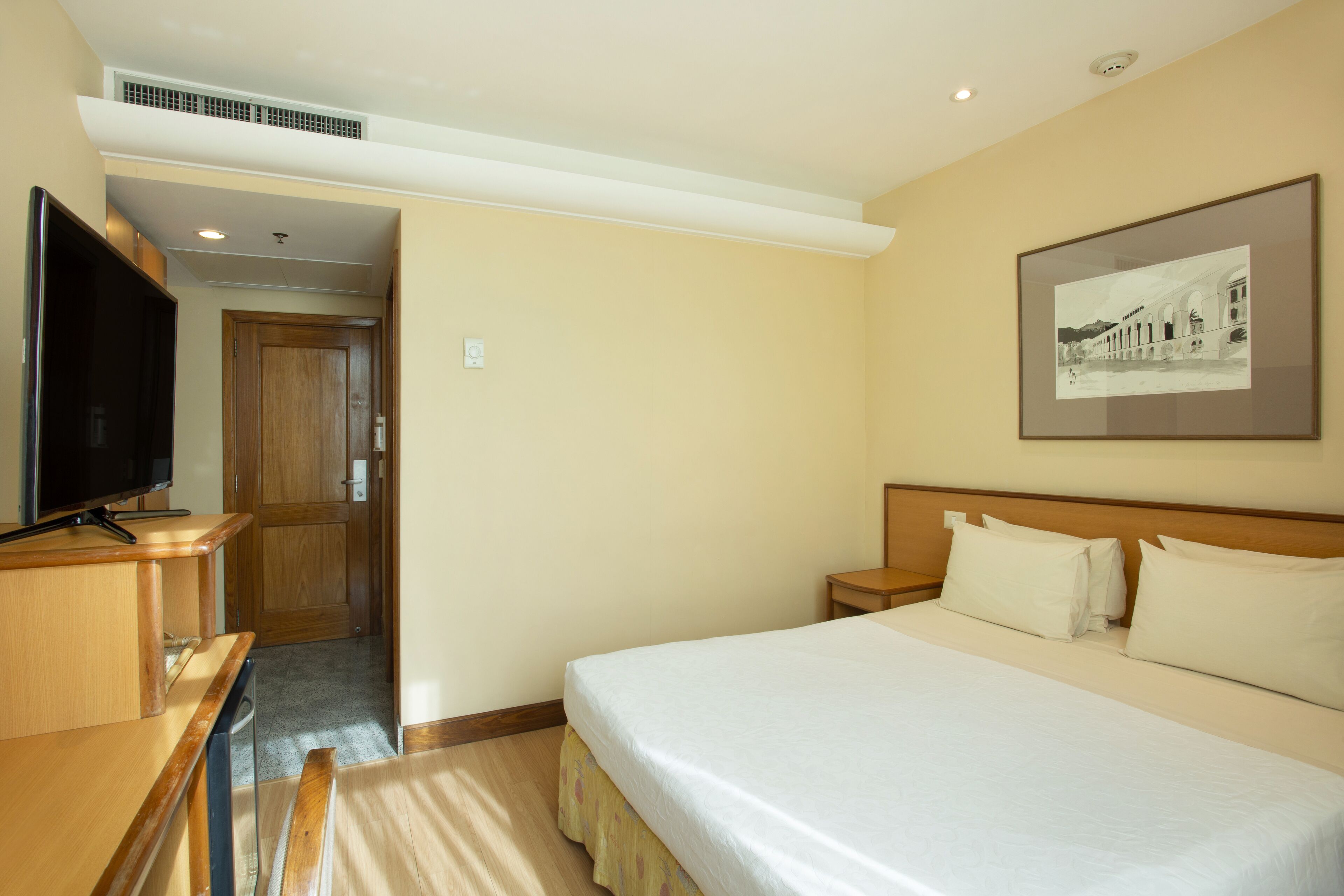 A hotel room with a bed, a television, a desk, and a framed picture on the wall.