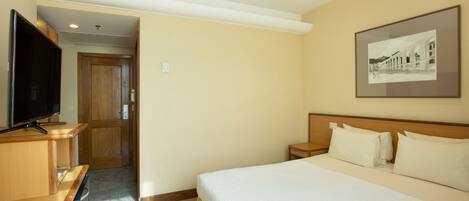 A hotel room with a bed, a television, a desk, and a framed picture on the wall.