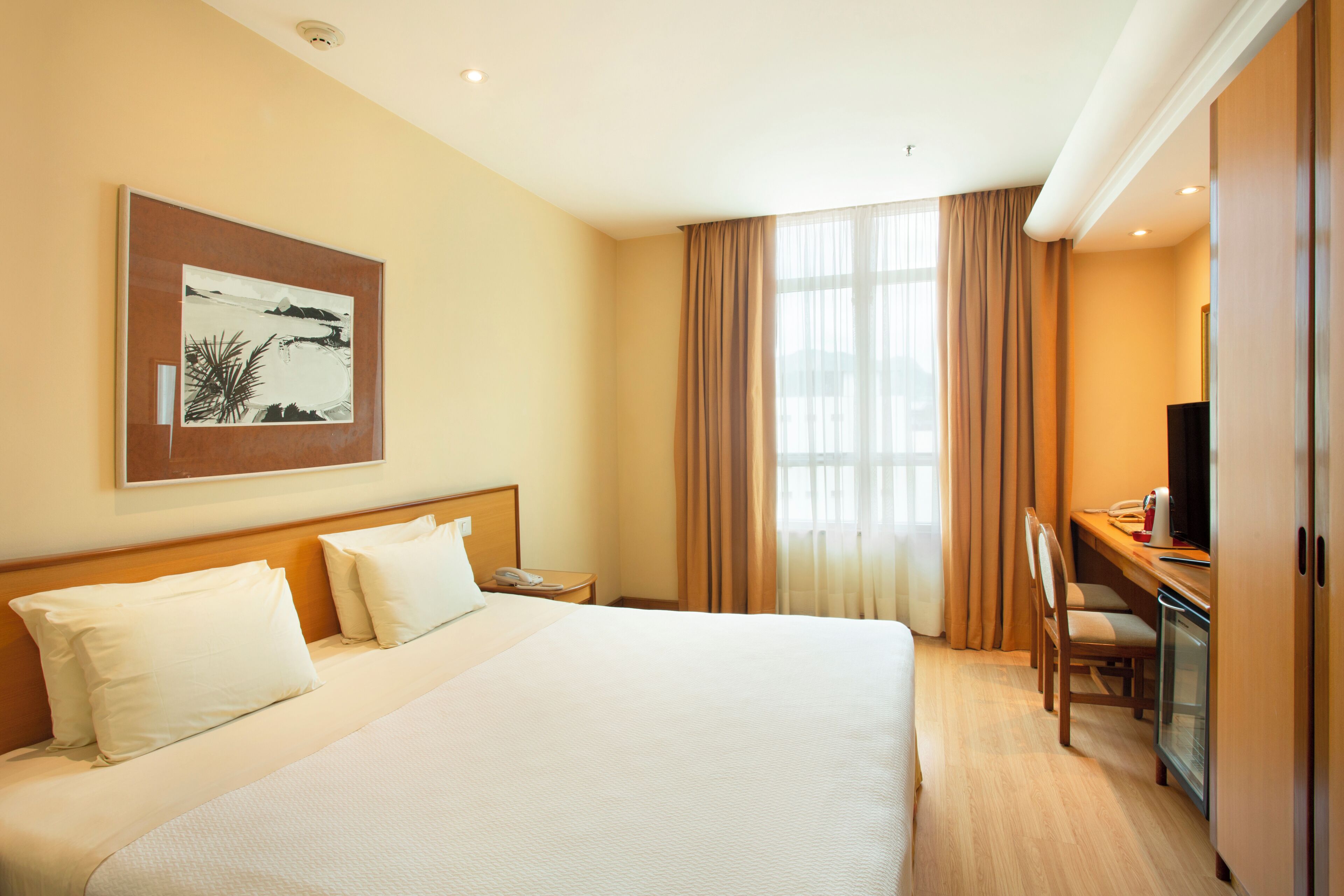 A hotel room with a large bed, a desk with a computer, a television, and a painting on the wall.