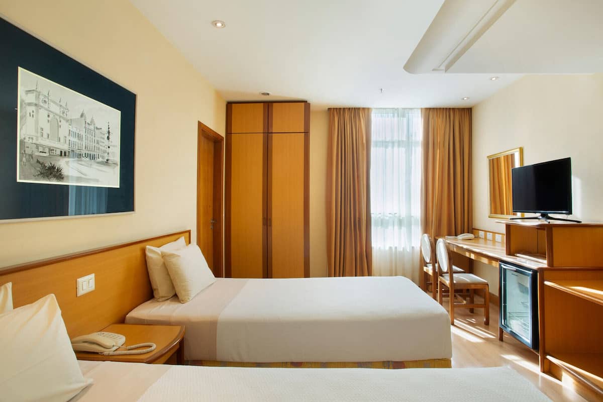A hotel room with two beds, a desk, a television, and a framed picture on the wall.