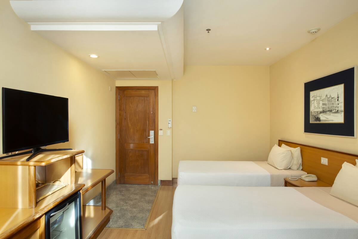 A hotel room with two beds, a TV, a desk with a computer, and a framed picture on the wall.