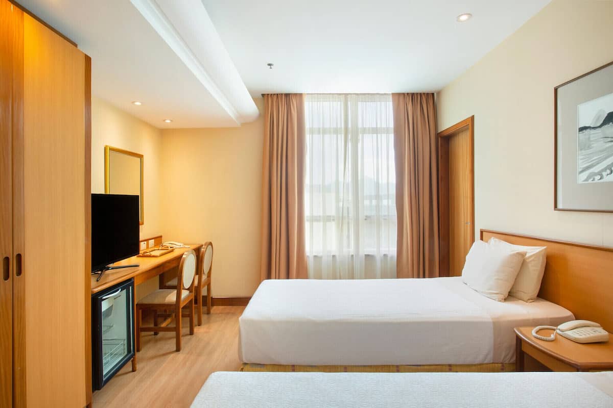 A hotel room with a bed, a desk with a television, a mini-fridge, and a phone.