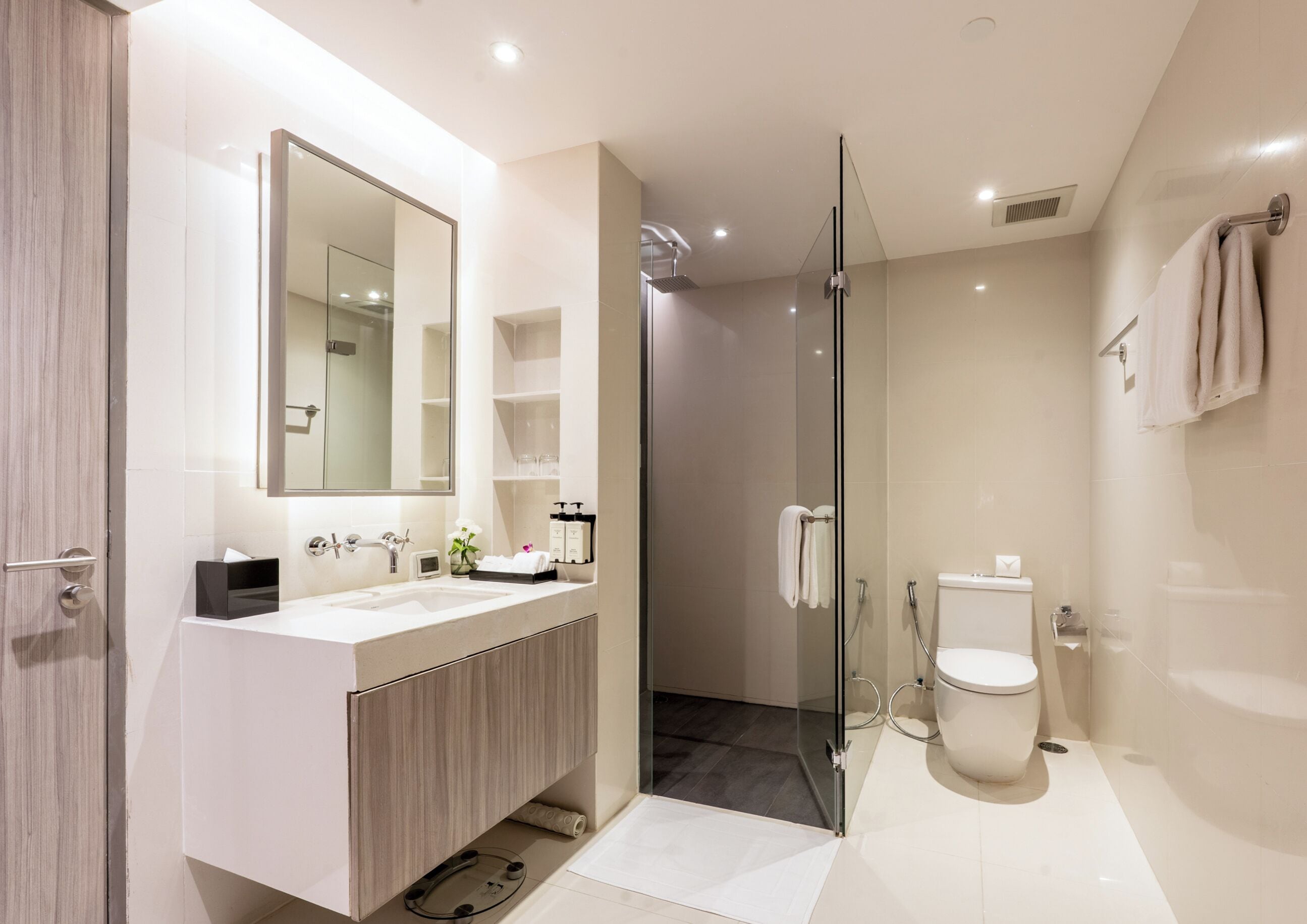 A modern bathroom with a glass-enclosed shower, a large mirror, and a vanity with a sink and storage.